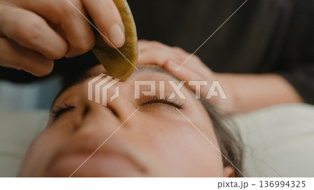 Relaxed woman enjoying jade facial massage in serene spa setting 136994325