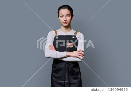 Portrait of young smiling female student in apron on gray background Portrait of young smiling female student in apron on gray background 136994936