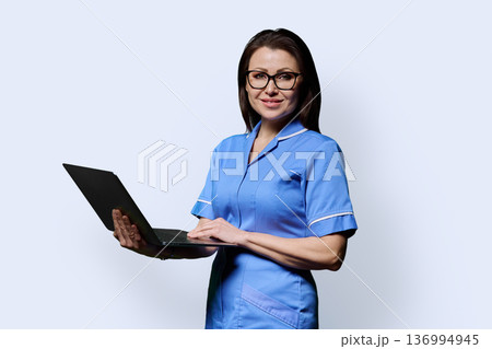 Female nurse holding laptop, looking at camera on white studio background Female nurse holding laptop, looking at camera on white studio background 136994945