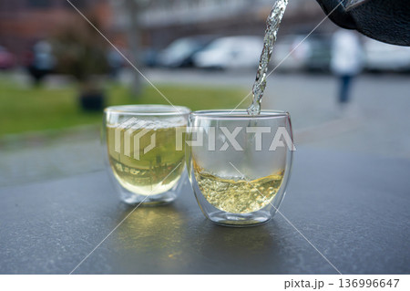 Pouring green tea into a glass from a metal kettle on blurred background, hot drink in teapot 136996647