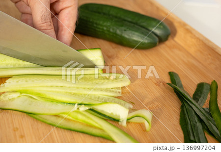 Slicing cucumbers with a large knife on wood cooking board close-up Slicing cucumbers with a large knife on wood cooking board close-up 136997204