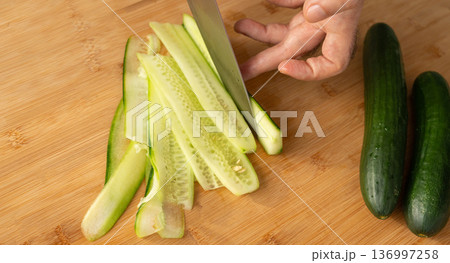 Slicing cucumbers with a large knife on wood cooking board close-up Slicing cucumbers with a large knife on wood cooking board close-up 136997258