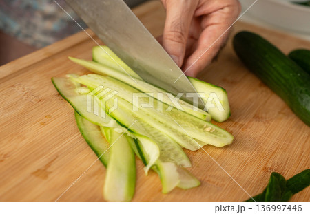 Slicing cucumbers with a large knife on wood cooking board close-up 136997446