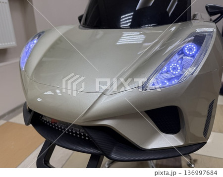 A close-up of a silver kids ride-on sports car with glowing blue LED headlights, childhood entertainment, luxury toy, modern design. 136997684