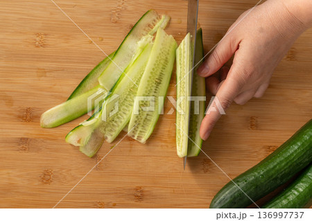 Slicing cucumbers with a large knife on wood cooking board close-up Slicing cucumbers with a large knife on wood cooking board close-up 136997737