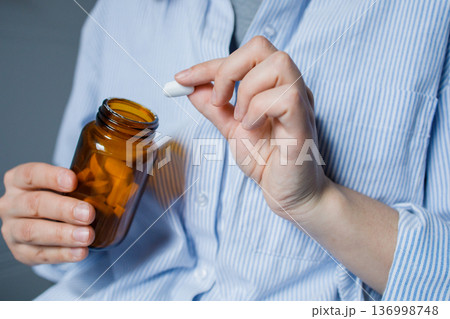 Woman taking one tablet from brown glass bottle with pills. Taking medication at home, disease prevention, taking antidepressants, vitamins, dietary supplements. Healthcare and medicine. 136998748