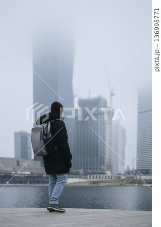 Man in winter coat overlooking a foggy city waterfront. Concept of a city winter activity 136998771