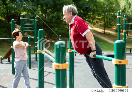 Senior man pulls up on crossbar in city park on sports ground Senior man pulls up on crossbar in city park on sports ground 136999691