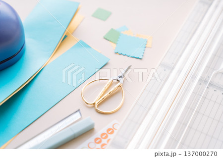 Craft workspace with paper cutter, scissors and colorful paper pieces on pastel background, DIY scrapbooking flat lay 137000270