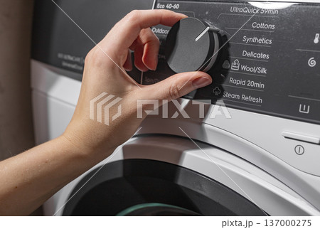 Hand selecting washing program on machine panel. Fingers turning control knob choosing cycle. Household appliance operation concept.. Hand selecting washing program on machine panel. Fingers turning control knob choosing cycle. Household appliance operation concept.. 137000275