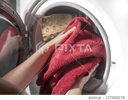 Hands inserting towels into dryer drum. Laundry placed inside drying machine appliance. Household care routine concept.. 137000278