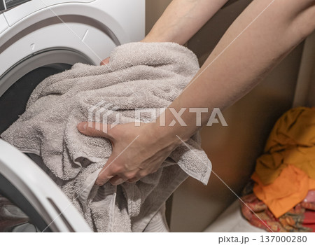 Hands loading laundry into washing machine drum. Towels placed inside appliance front loader. Household cleaning routine concept.. 137000280
