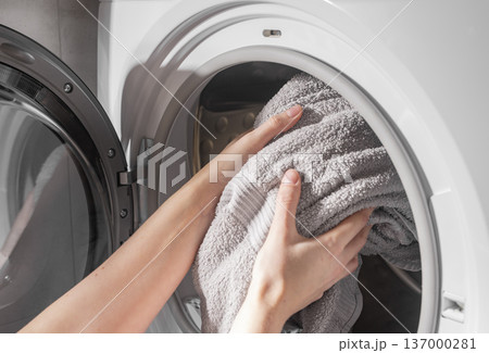 Hands placing towels into washing machine drum. Laundry loaded inside appliance front loader. Domestic cleaning routine concept.. Hands placing towels into washing machine drum. Laundry loaded inside appliance front loader. Domestic cleaning routine concept.. 137000281