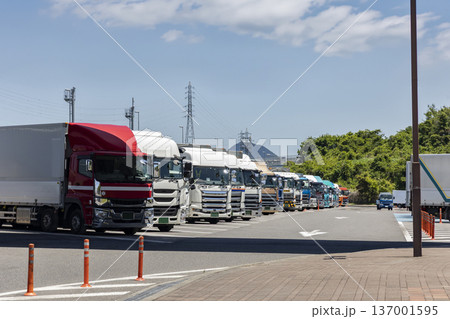 青空の下、高速道路のサービスエリアに整列して駐車された大型トラックの列 137001595