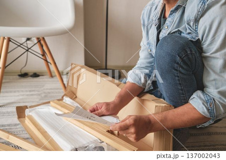 Man unboxing flat pack furniture and reading instructions 137002043