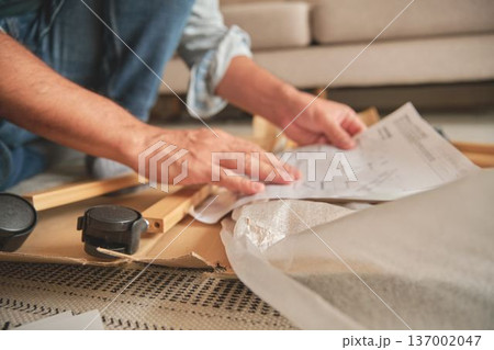 Person assembling flat pack furniture reading instructions at home 137002047
