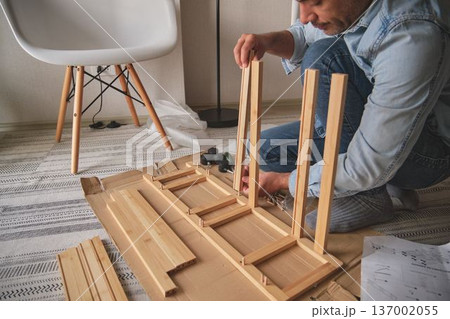 Man assembling furniture parts using screwdriver and instructions 137002055