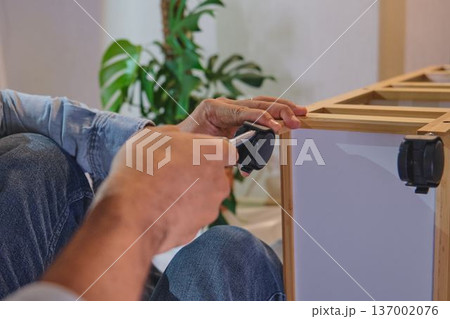 Person assembling furniture installing wheel casters with screwdriver 137002076