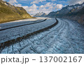A vast glacier Aletsch Glacier in Switzerland Aps flows between rugged mountains on a bright summer day. The beautiful landscape showcases stunning natural formations and greenery. Aerial drone view. 137002167