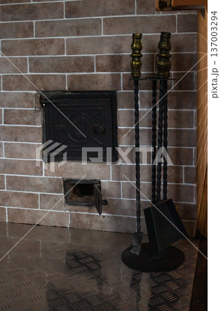 Traditional wood-burning fireplace. Beige brick construction with burning fire. Accessories stand. Cozy heating solution for home Traditional wood-burning fireplace. Beige brick construction with burning fire. Accessories stand. Cozy heating solution for home 137003294