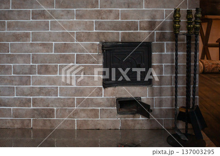 Wood burning fireplace in beige brick. Fire tools on decorative stand. Open door showing flames. Cozy country house interior Wood burning fireplace in beige brick. Fire tools on decorative stand. Open door showing flames. Cozy country house interior 137003295