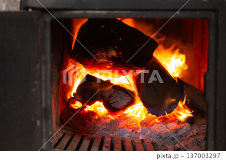Traditional brick fireplace with flames. Open firebox with burning wood. Fireplace accessories and metal hearth. Traditional brick fireplace with flames. Open firebox with burning wood. Fireplace accessories and metal hearth. 137003297