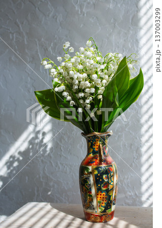 Spring flowers lily of the valley in decorative vase. Sunlight on windowsill. White bell-shaped blooms with large green leaves 137003299
