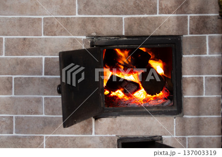Open fireplace with flames and burning wood. Brick stove with tools. Traditional home heating. Warm rustic atmosphere Open fireplace with flames and burning wood. Brick stove with tools. Traditional home heating. Warm rustic atmosphere 137003319