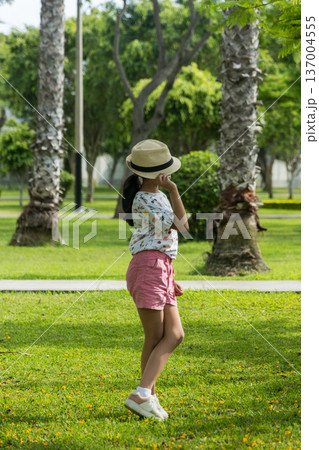 A young girl wearing a straw hat and a white shirt is standing in a grassy field A young girl wearing a straw hat and a white shirt is standing in a grassy field 137004555