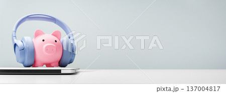Piggy bank with headphones on laptop, podcast and fintech concept Piggy bank with headphones on laptop, podcast and fintech concept 137004817