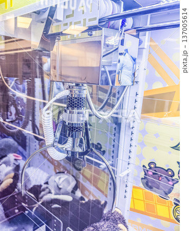 Close up of a claw machine grabber in a brightly lit arcade, attempting to pick up a stuffed toy prize from a pile. 137005614