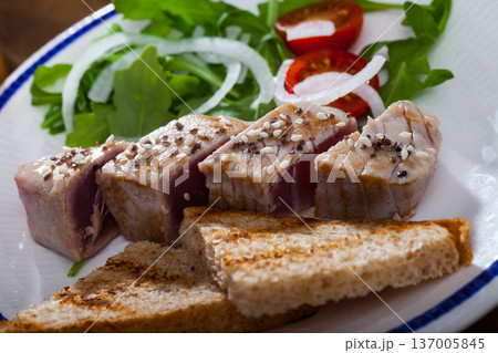 Tasty lightly fried tuna, served toasted bread and greens at plate Tasty lightly fried tuna, served toasted bread and greens at plate 137005845
