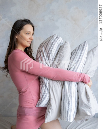 woman holds pile of pillows in her hands. pillows are in different colors, look like stack.  137006927