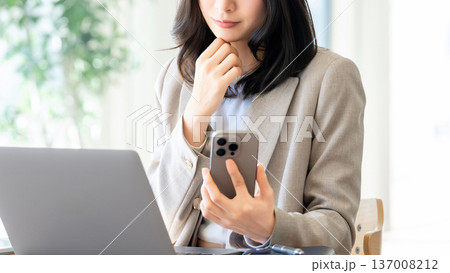 スマートフォンを見ながら考える女性・ビジネスウーマン スマートフォンを見ながら考える女性・ビジネスウーマン 137008212