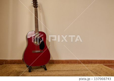 Red Acoustic Guitar Leaning Against Wall on Woven Rug in Minimal Interior 137008743