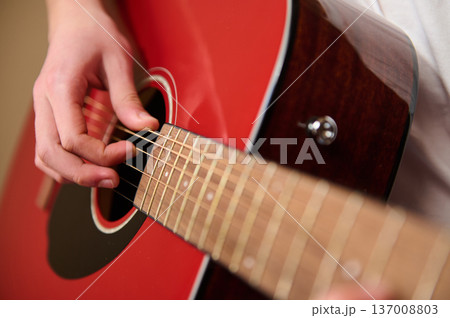 Close-Up Of Hand Playing Red Acoustic Guitar Focusing On Strings And Frets 137008803