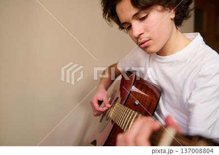 Teen Boy Playing Acoustic Guitar Indoors Practicing Music With Focused Expression 137008804