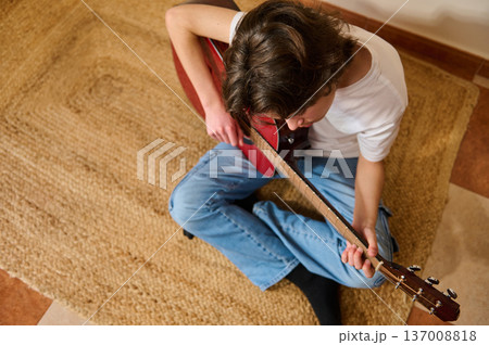 Teenager Playing Acoustic Guitar at Home Sitting on Rug Practicing Music Teenager Playing Acoustic Guitar at Home Sitting on Rug Practicing Music 137008818