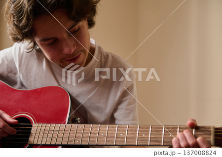 Teen Boy Playing Red Acoustic Guitar at Home Practicing Chords and Learning Music 137008824