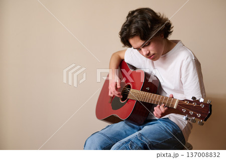 Teen Boy Playing Acoustic Guitar Indoors While Practicing Music and Focusing on Strumming 137008832