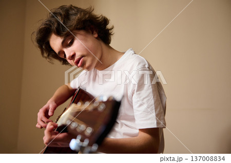 Teen Playing Acoustic Guitar at Home - Young Musician Practicing in Casual Portrait Teen Playing Acoustic Guitar at Home - Young Musician Practicing in Casual Portrait 137008834
