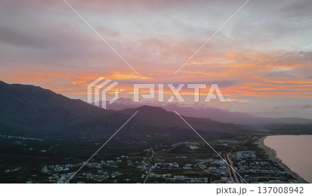Aerial panoramic view of Crete coastline at twilight with colorful pre-sunset sky, valley with fields and villages, mountain ridge, and reflective sea bay Aerial panoramic view of Crete coastline at twilight with colorful pre-sunset sky, valley with fields and villages, mountain ridge, and reflective sea bay 137008942
