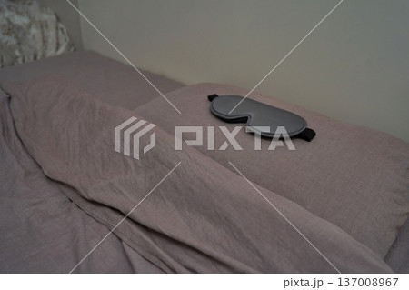 Gray sleep mask resting on neatly made bed with soft gray linens in calm bedroom setting Gray sleep mask resting on neatly made bed with soft gray linens in calm bedroom setting 137008967