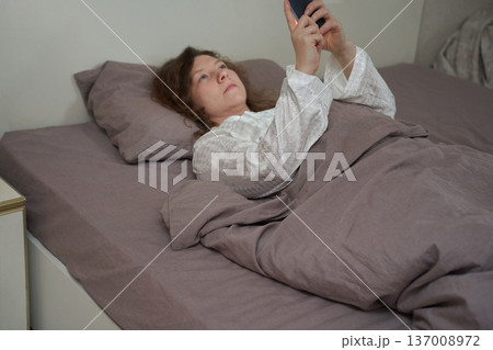 Caucasian mature female in bed using smartphone for relaxation or communication 137008972