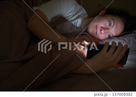 Caucasian female adult lying in bed using smartphone at night for relaxation or connection 137008982