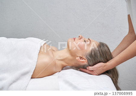 Mature caucasian woman relaxing during head massage therapy session in a spa setting for stress Mature caucasian woman relaxing during head massage therapy session in a spa setting for stress 137008995