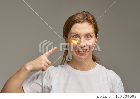 Young caucasian female applying gold eye mask for skincare routine and facial rejuvenation 137009005