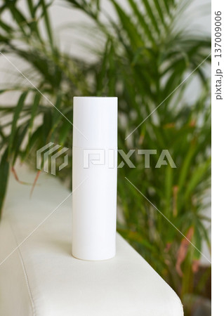 Minimalist white cylindrical container on beige surface with green plant background for skincare 137009006