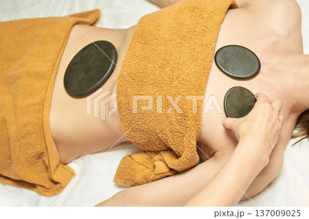 Young Caucasian Female Enjoying Hot Stone Therapy For Relaxation And Wellness At Spa 137009025
