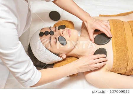Young Asian Female Receiving Relaxing Hot Stone Massage At Spa For Stress Relief And Rejuvenation 137009033